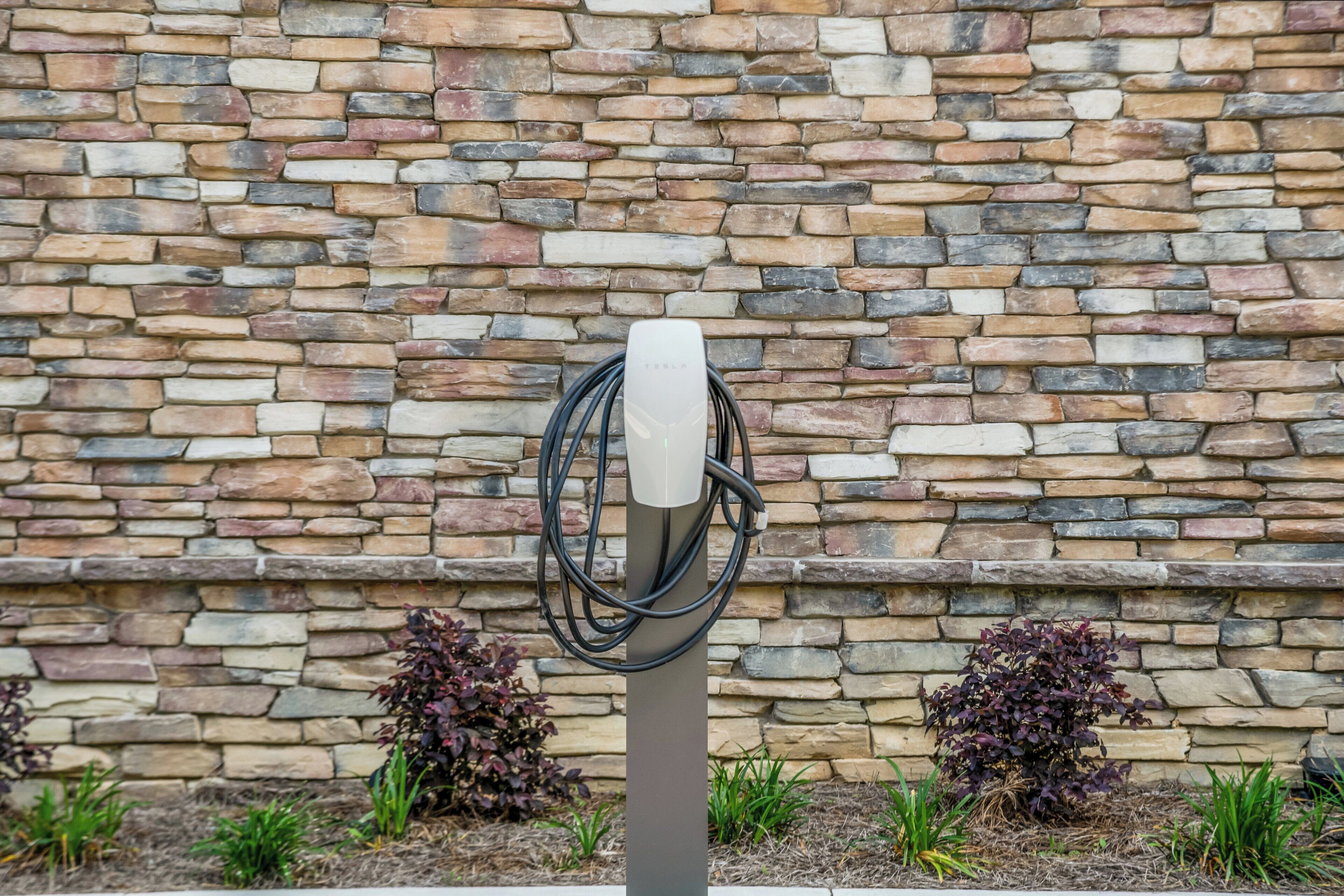 A charging station with a cable coiled around it, set against a stone wall background.