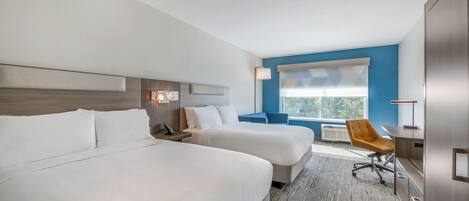 A hotel room with two beds, a desk, a chair, a window, and a lamp.