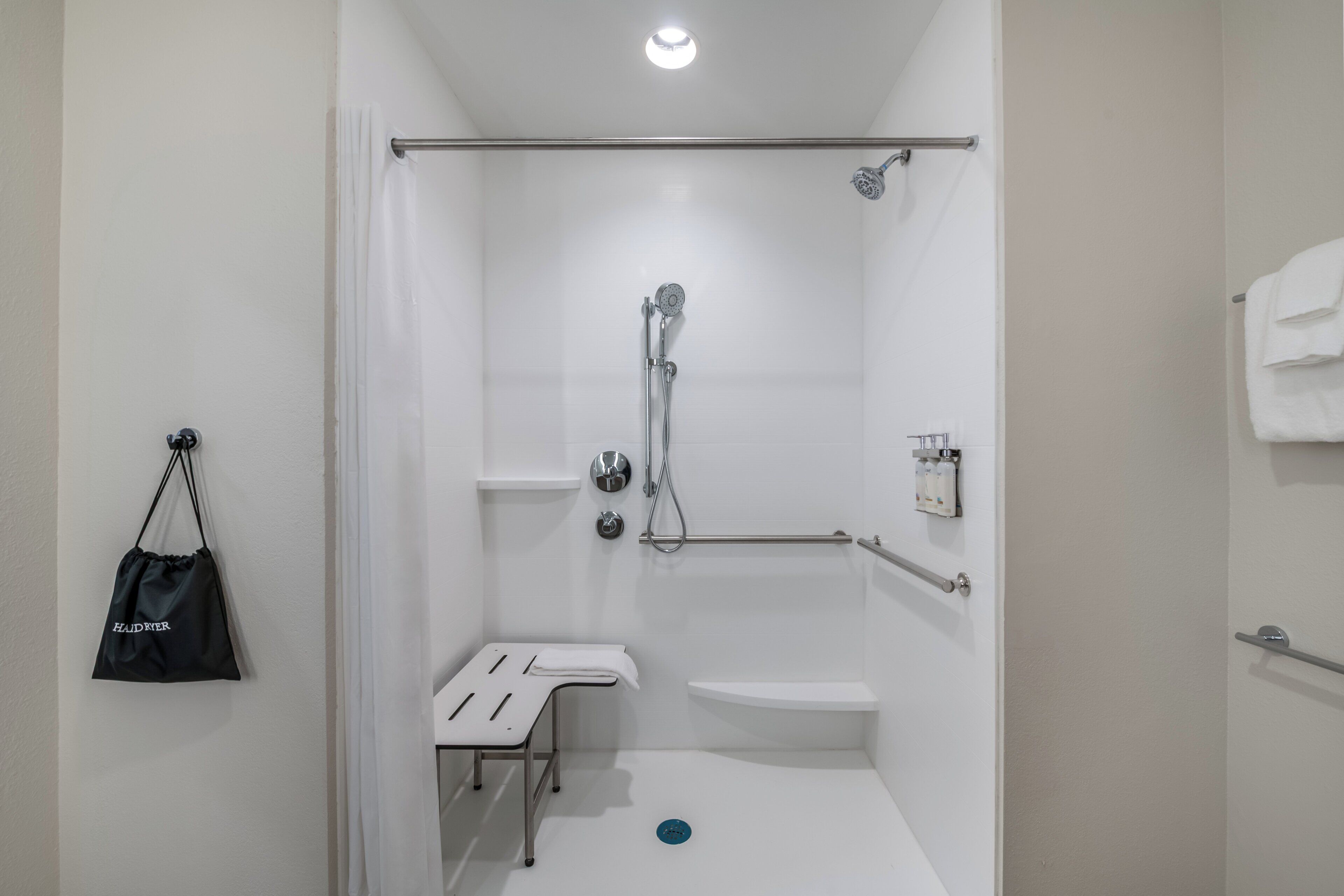 A shower with a handheld showerhead, a grab bar, a white bench, and a towel rack.