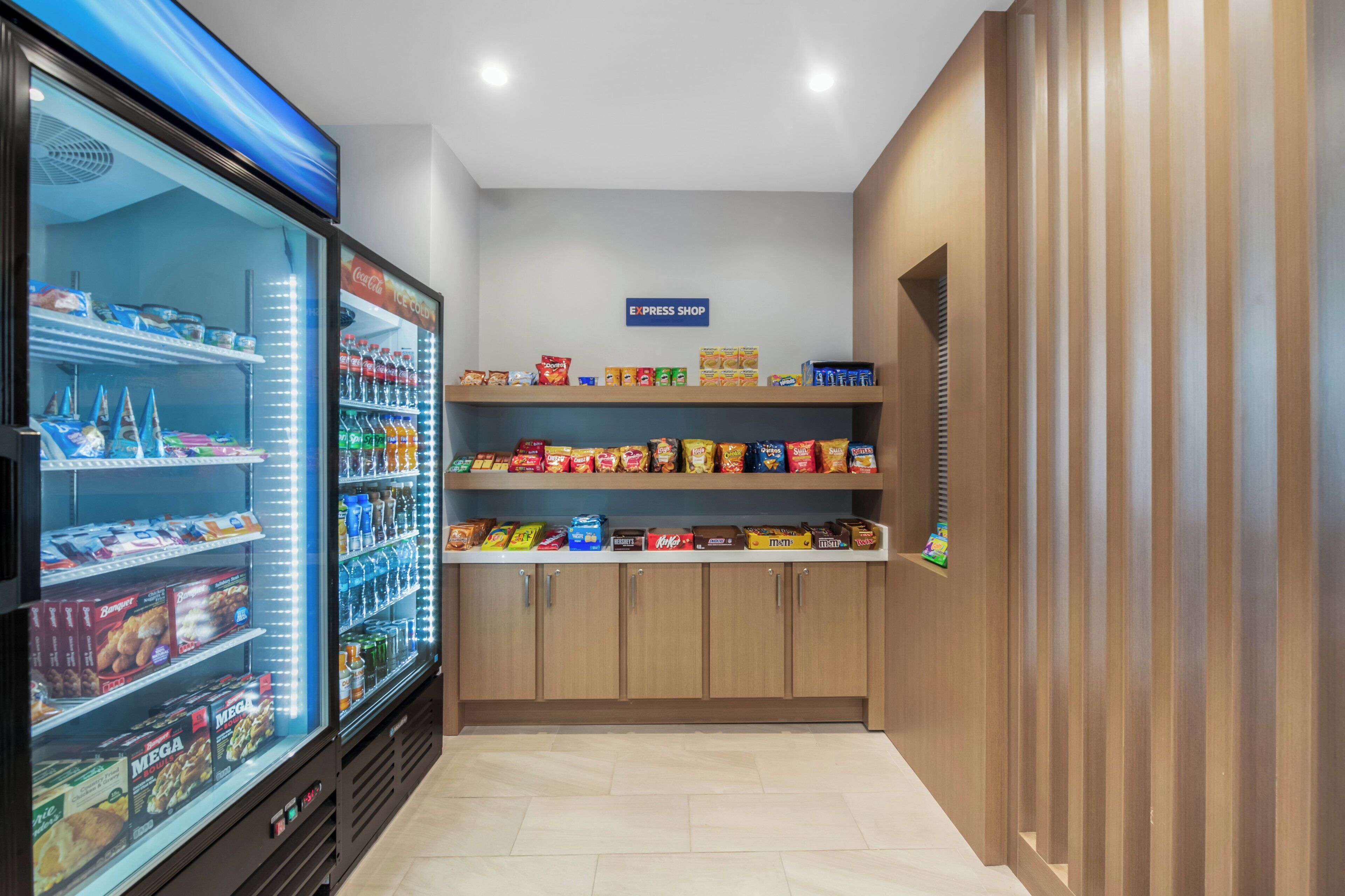 A clean, well-lit room with a refrigerator stocked with snacks and beverages, a shelf with packaged goods, and a sign indicating an express shop.