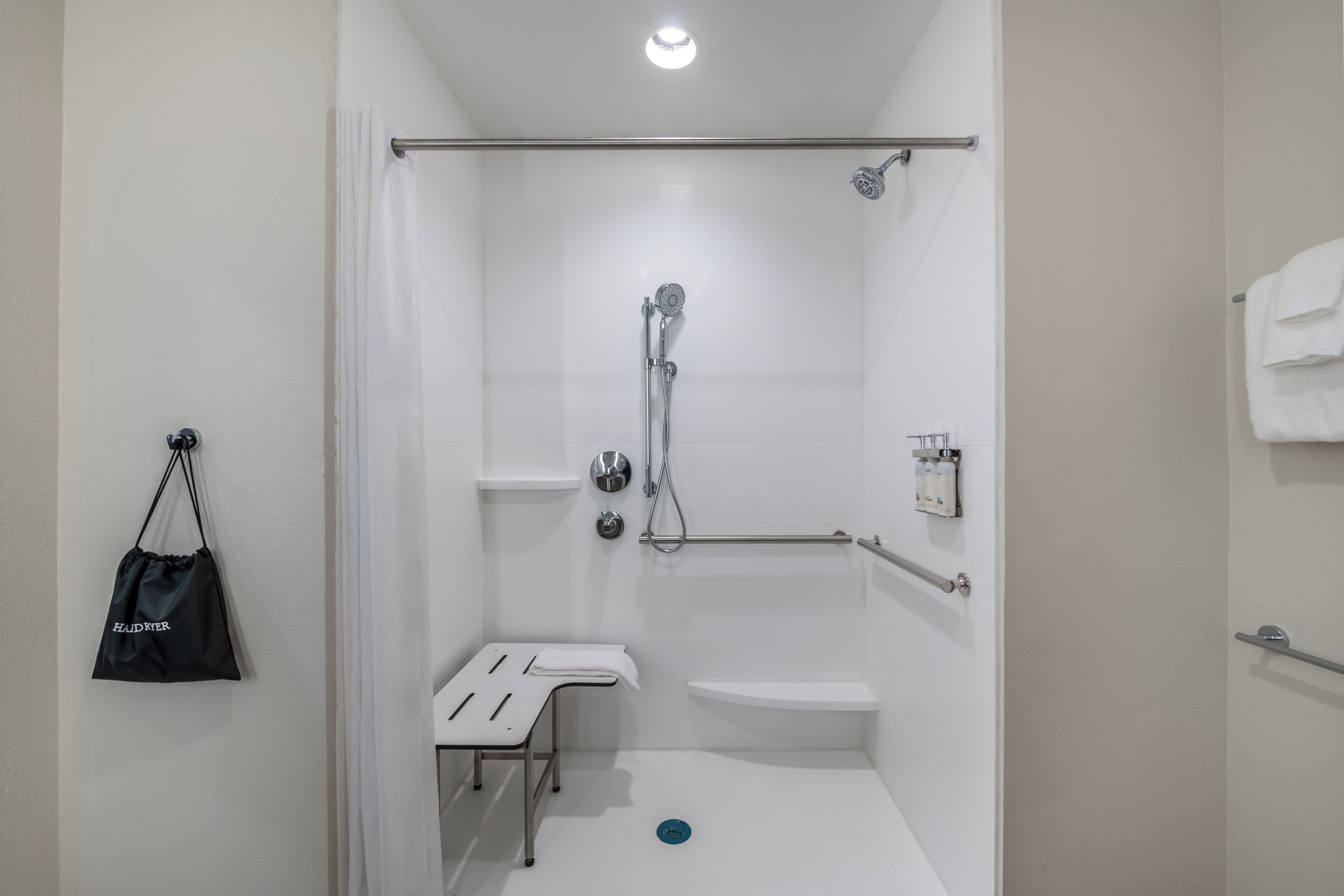 A shower with a handheld showerhead, a grab bar, and a white sink.