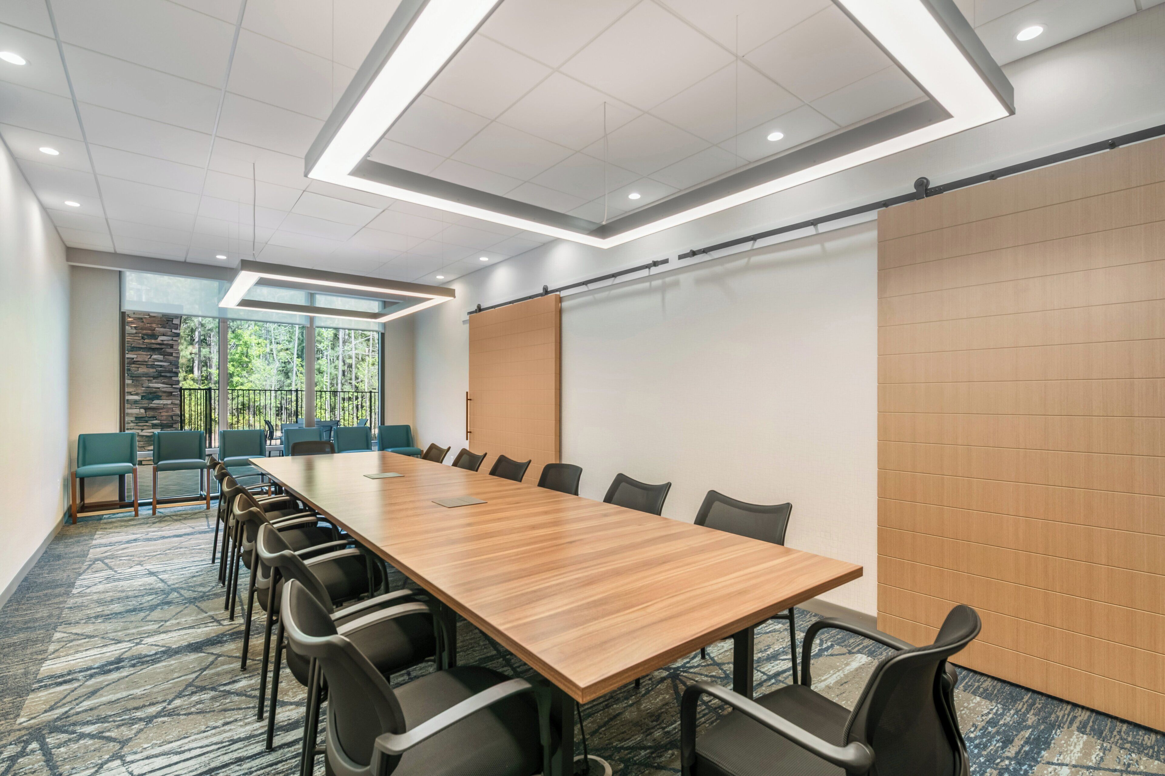 Une salle de conférence dotée d’une longue table, de chaises, d’un écran de projection et offrant une vue sur les arbres à travers de grandes fenêtres.