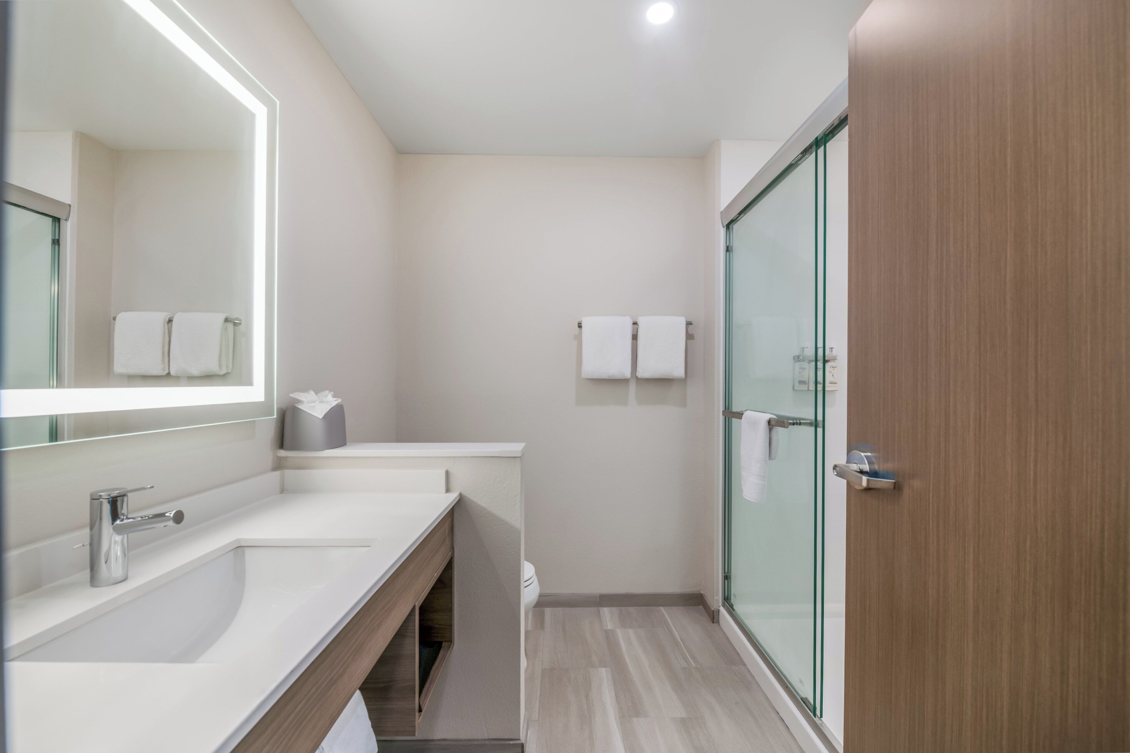 Un baño moderno con un espejo grande, dos lavamanos, una cabina de ducha de vidrio y una puerta de madera.