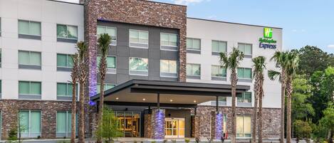 A Holiday Inn Express hotel with a modern design, featuring a stone facade, multiple windows, and a covered entrance area.