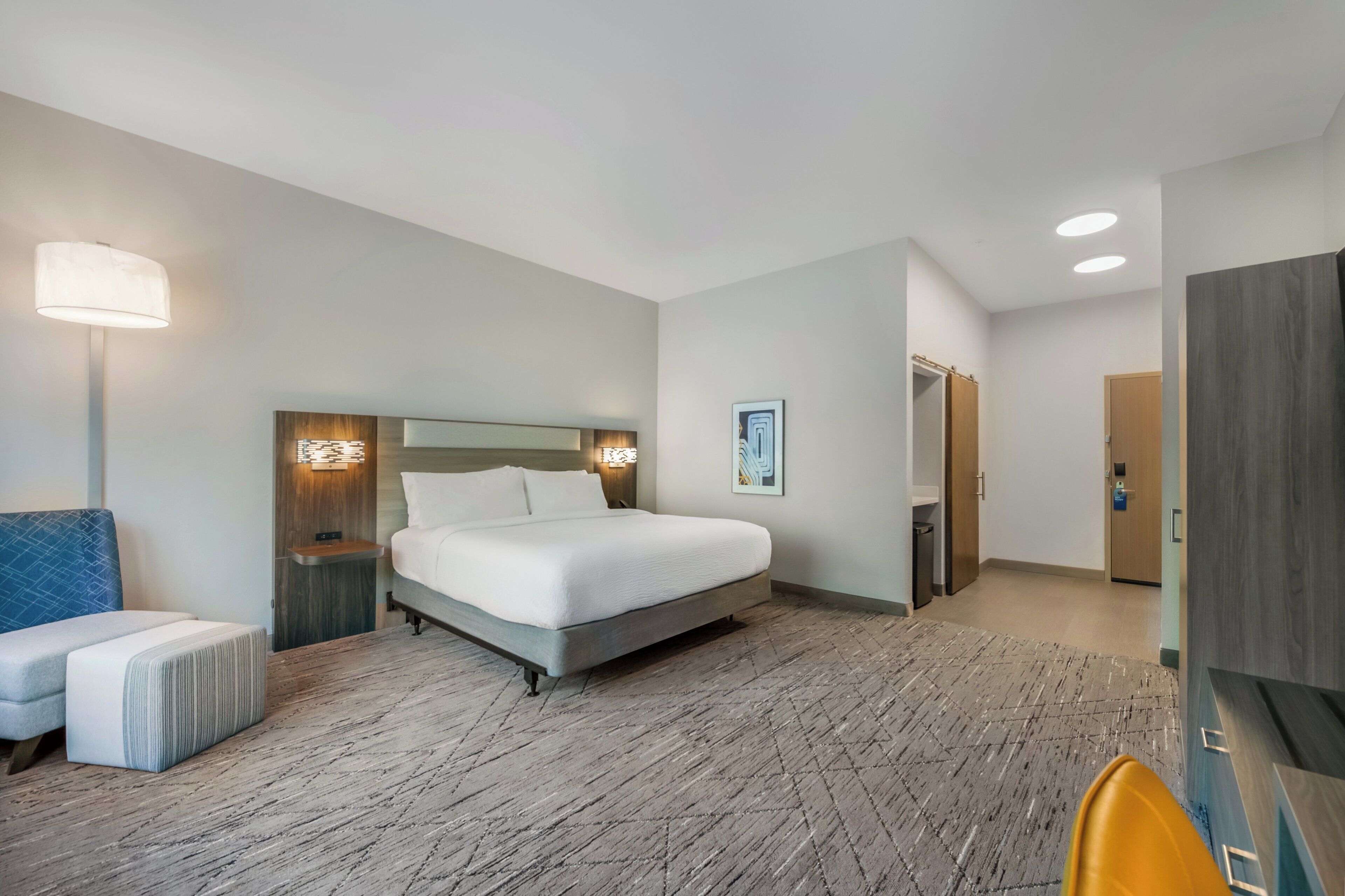 Una habitación de hotel con cama, mesitas de noche, lámpara, sillón y armario.
