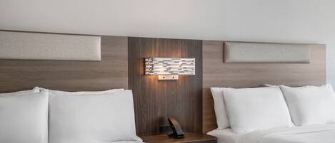 Habitación de hotel con dos camas, una mesita de noche con lámpara, y una lámpara de pared.