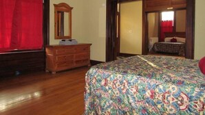 A bedroom with a wooden dresser, a bed with a floral bedspread, a mirror, and a red curtain. - Peabody Backhouse 5 (Memphis)