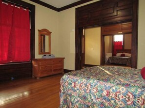 Una camera da letto con un comò in legno, un letto con copripiumino floreale, uno specchio e una tenda rossa.