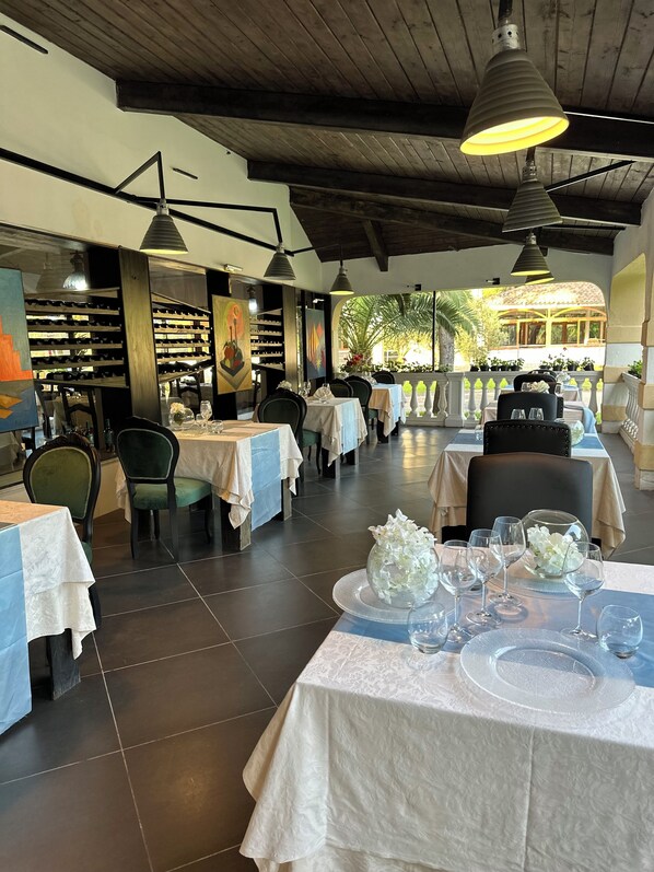 Ein Restaurant mit gedeckten Tischen, das ein modernes Interieur mit Holzbalken und Pendelleuchten zeigt.