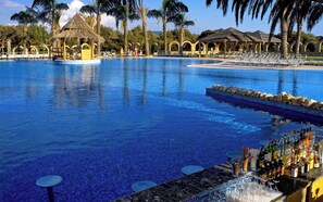 Ein großer Pool mit Liegestühlen und Sonnenschirmen, umgeben von Palmen und einer Bar.