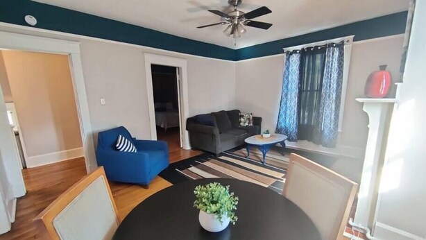 Una sala de estar con ventilador de techo, un sofá azul, un sofá gris, una pequeña mesa redonda y una planta en maceta.