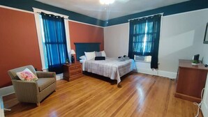 Un dormitorio con cama, una silla, cómoda y ventana con cortinas.