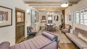 A cozy living room with a sofa, a dining table, and a chair. There is a wooden door and a window with a view. - Mid-Century Modern Taos Home w/ Hot Tub & Fire Pit (Taos)
