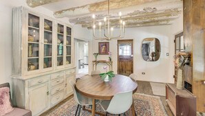 A dining room with a wooden table, white chairs, a chandelier, a cabinet with glass doors, and a patterned rug. - Mid-Century Modern Taos Home w/ Hot Tub & Fire Pit (Taos)
