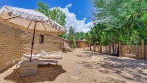A patio area with a brick wall, a covered seating area, and a gravel path. - Mid-Century Modern Taos Home w/ Hot Tub & Fire Pit (Taos)