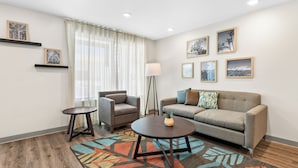 A modern living room with a sofa, armchair, coffee table, and a floor lamp. - Woodspring Suites Ceres - Modesto (Ceres)