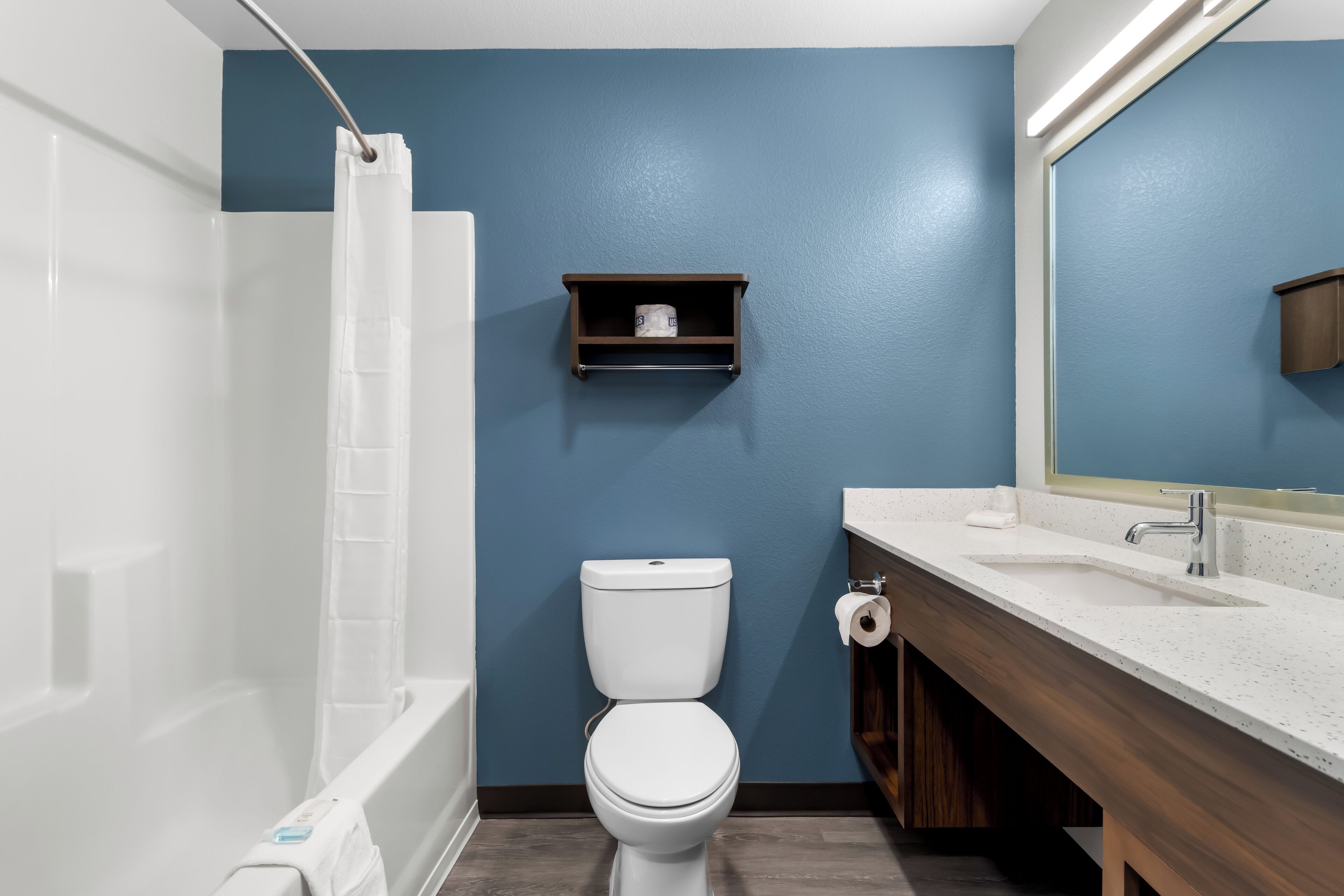 A bathroom with a white toilet, a bathtub, a wooden vanity with a sink, and a blue wall.