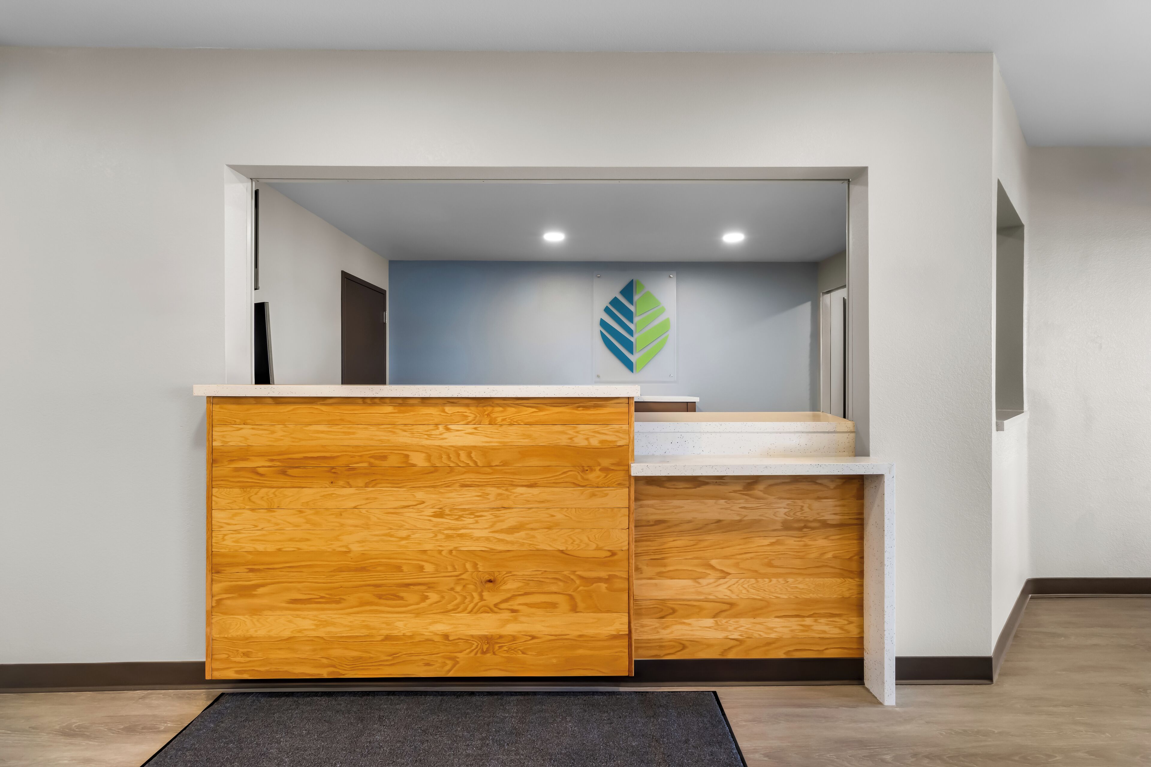 Zona d'e recepció amb un taulell de fusta, una paret blava amb un logotip de fulla i una escala que mena a un pis superior.