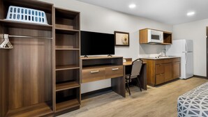 A compact room with a wooden desk, a television, a microwave, and a refrigerator. - Woodspring Suites Ceres - Modesto (Ceres)