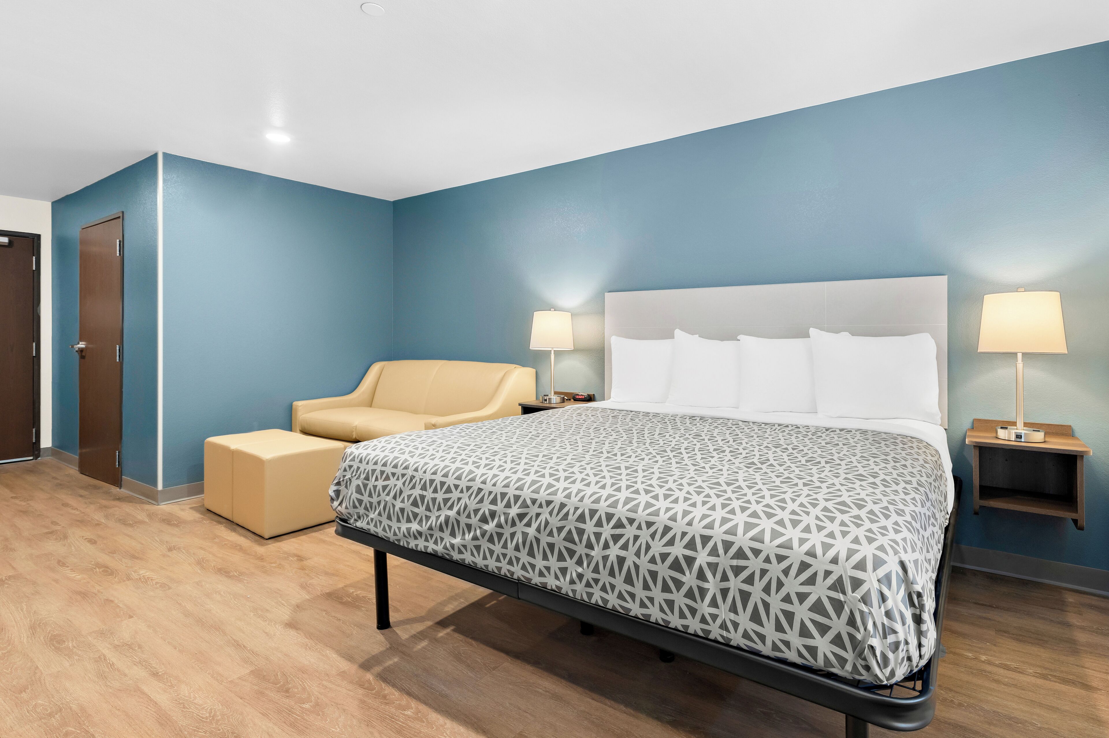 A hotel room with a large bed, a chair, two bedside tables with lamps, and a door.