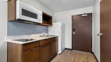 Une cuisine compacte avec des meubles en bois, un plan de travail blanc, un four à micro-ondes encastré et un réfrigérateur blanc.