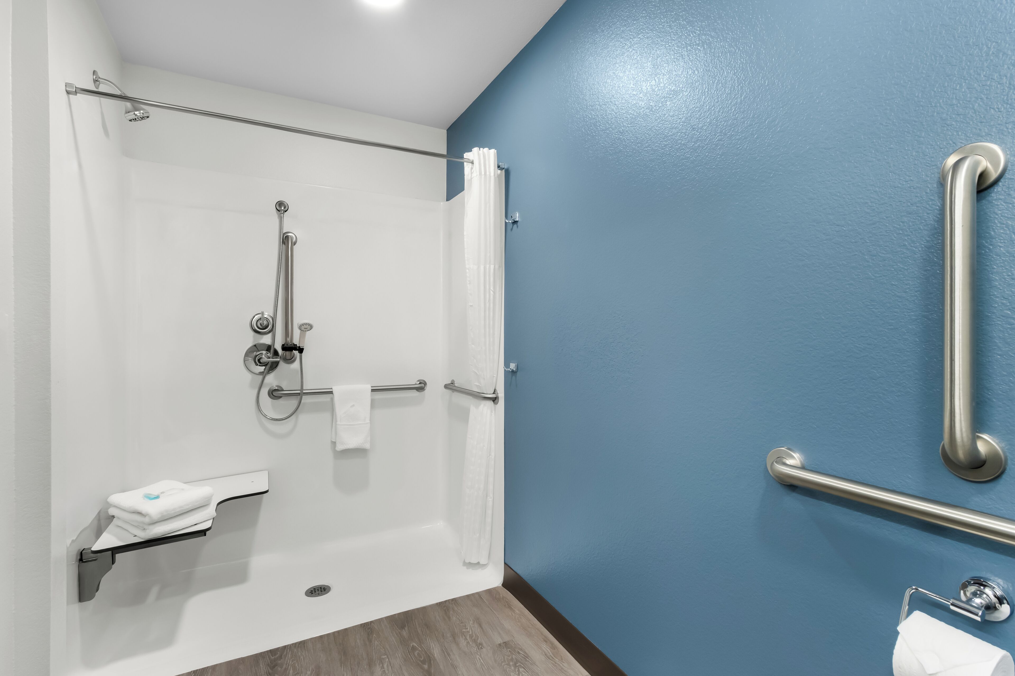 A bathroom with a shower, grab bars, a towel rack, and a toilet paper holder.