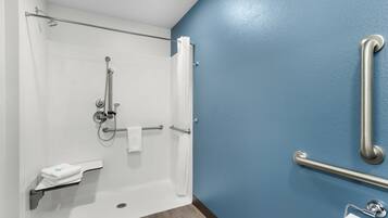 A bathroom with a shower, grab bars, a towel rack, and a toilet paper holder.