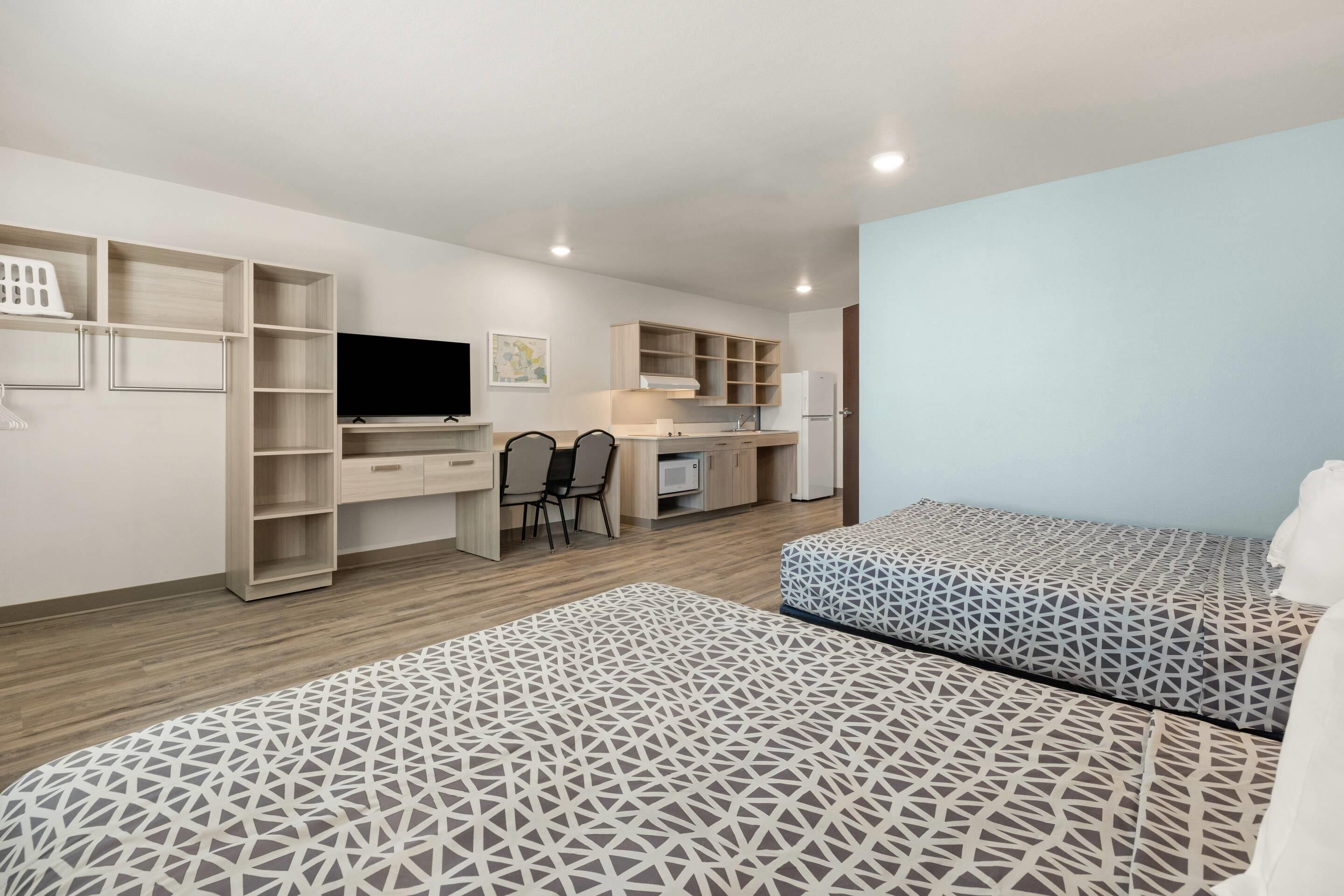 Ein modernes Zimmer mit einem Bett, einem Schreibtisch, einem Sessel, einem Fernseher und einer Küchenzeile.