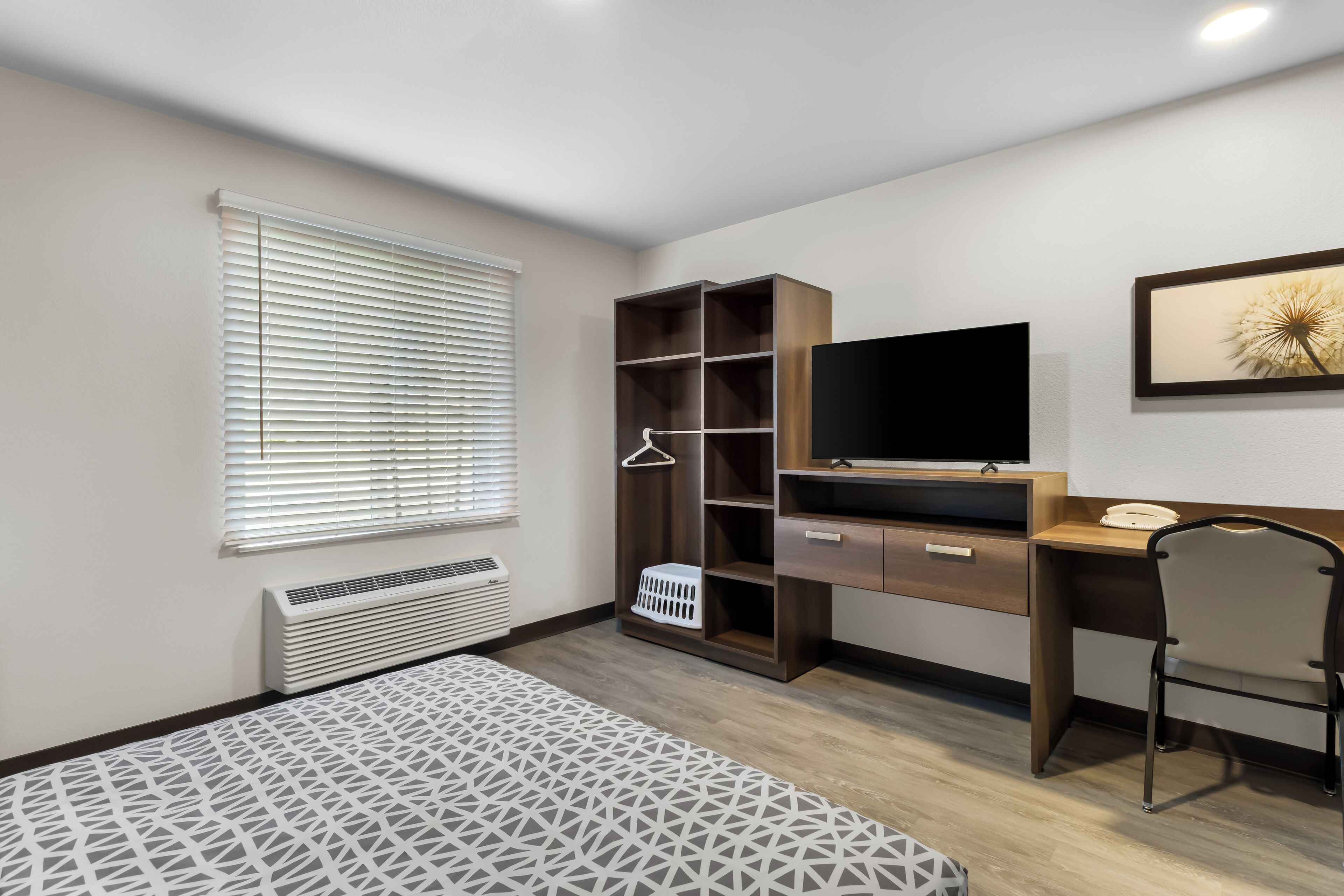 A bedroom with a bed, a desk, a chair, a wardrobe, a TV, and a window with blinds.