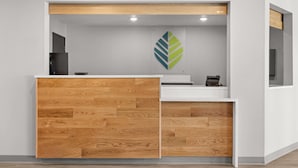 A reception desk with a wooden panel design, a logo on the wall, and a small printer. - Woodspring Suites Ceres - Modesto (Ceres)