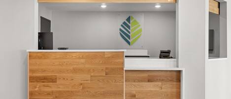 A reception desk with a wooden panel design, a logo on the wall, and a small printer.