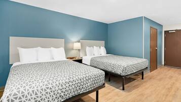 A hotel room with two beds, a nightstand, a lamp, and a door.