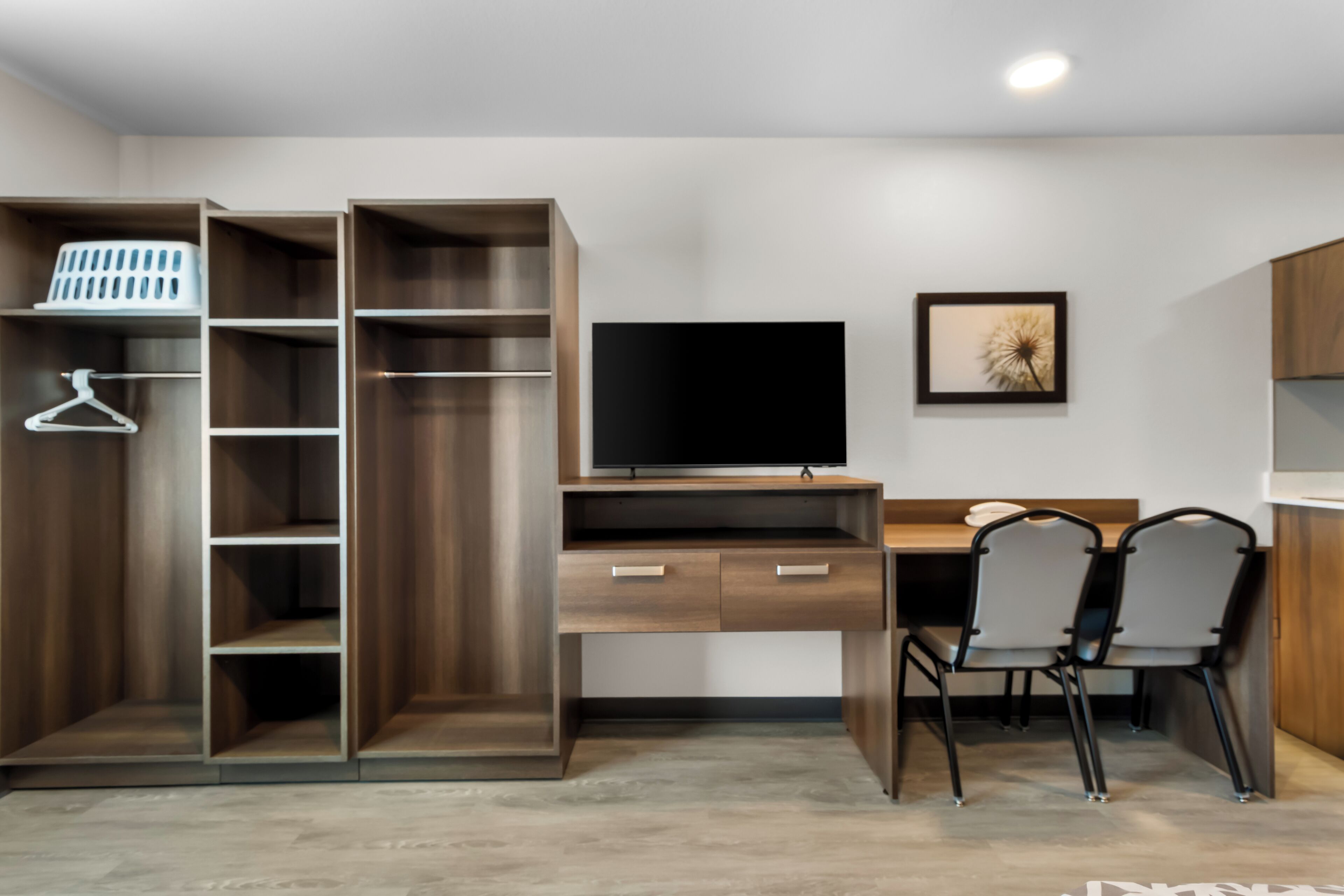 A modern room with a wooden desk, two chairs, a TV, and a wardrobe with shelves and hanging space.