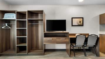 A modern room with a wooden desk, two chairs, a TV, and a wardrobe with shelves and hanging space.