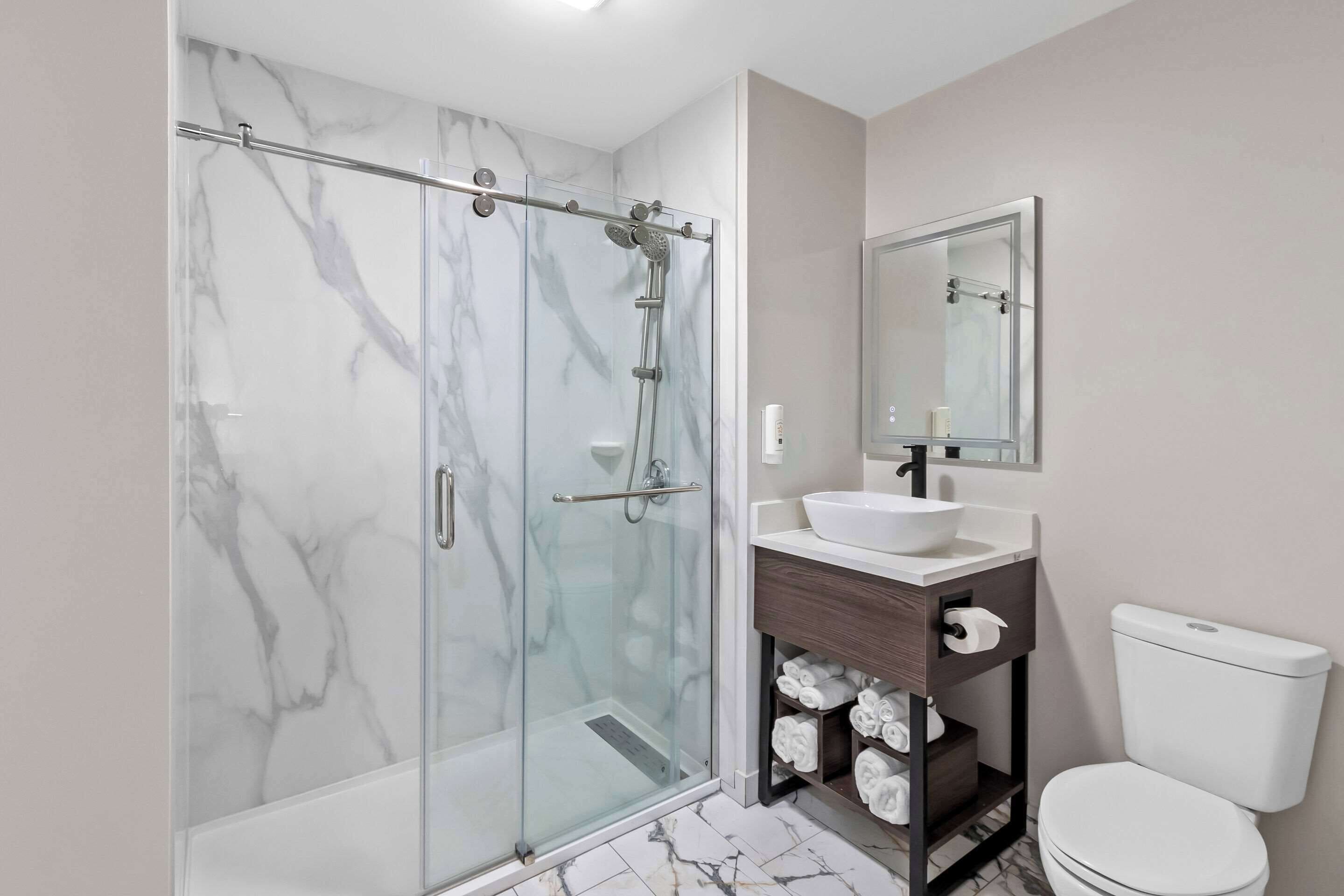 A modern bathroom with a glass-enclosed shower, a white sink, a wooden vanity, and a toilet.