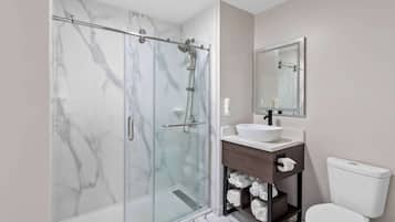 A modern bathroom with a glass-enclosed shower, a white sink, a wooden vanity, and a toilet.
