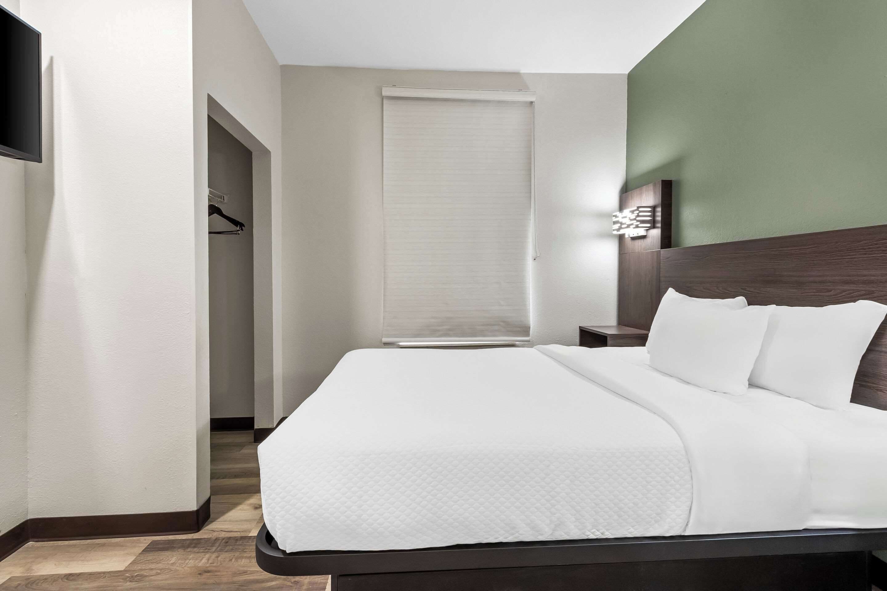 Ein Hotelzimmer mit Bett, Nachttisch, Wandleuchte und Schrank mit Kleiderstange.