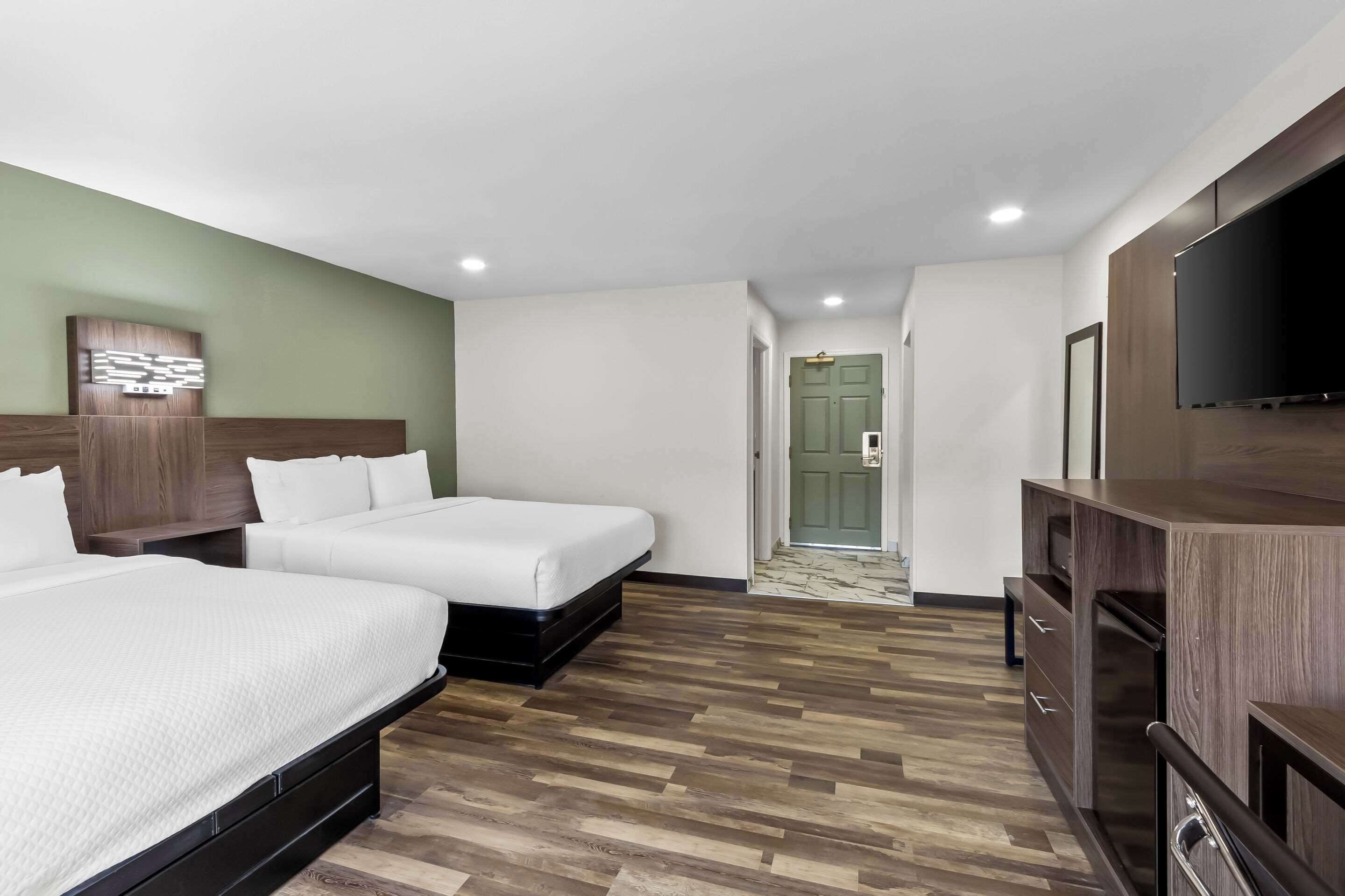 A hotel room with two beds, a TV, a wooden cabinet, and a green door.