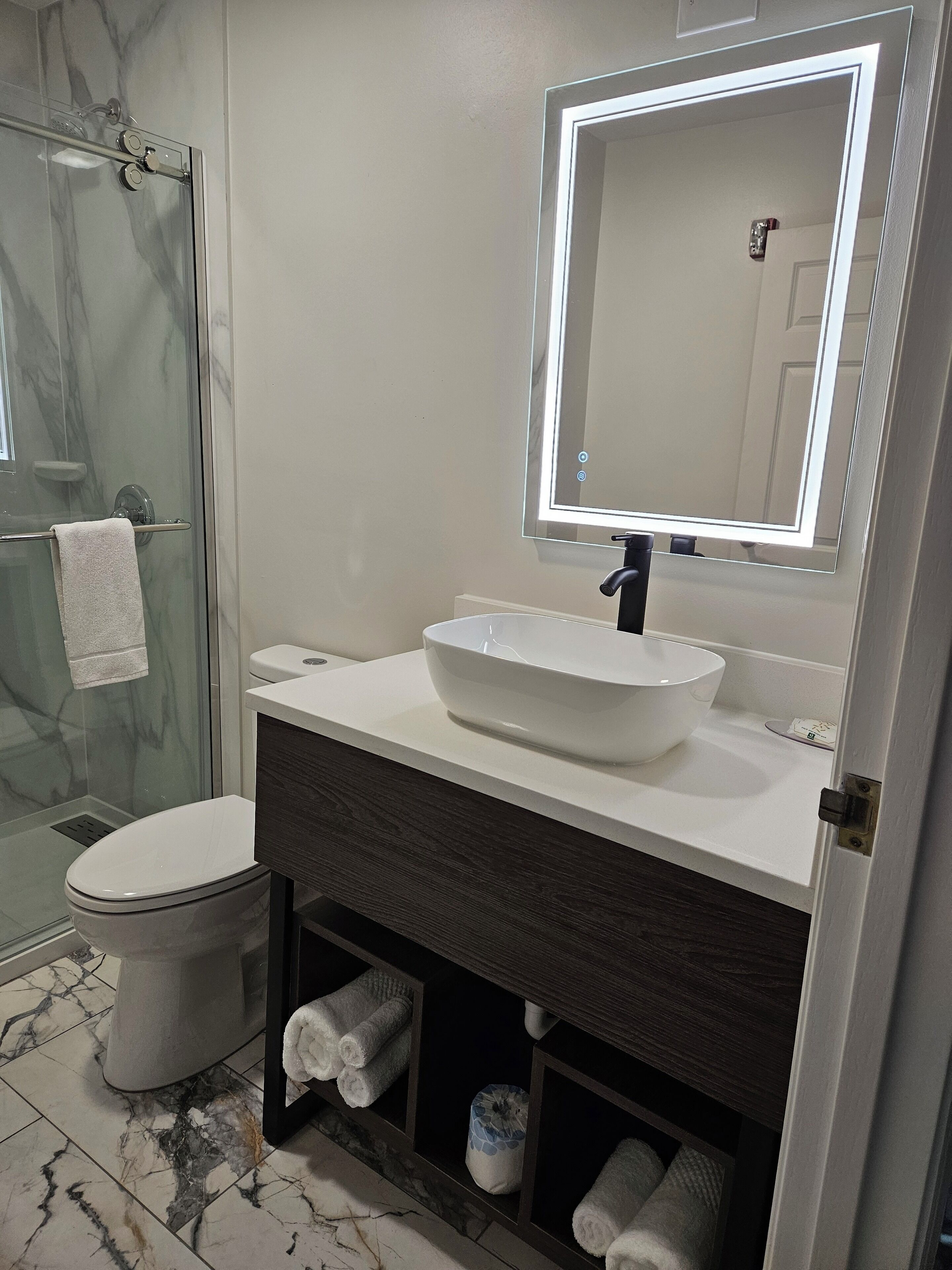 Ein Badezimmer mit Glasdusche, Toilette in Weiß, Waschbecken in Weiß und einem großen Spiegel darüber sowie einem dunkelholzfarbenen Waschtisch.
