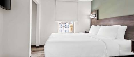 Een moderne hotelkamer met een groot bed, een flatscreen televisie aan de muur en een raam met uitzicht op gebouwen.