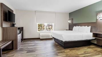 A modern hotel room with a large bed, a flat-screen TV, a built-in bench, and a window with a view of trees.