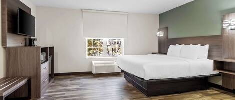 A modern hotel room with a large bed, a flat-screen TV, a built-in bench, and a window with a view of trees.