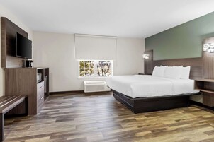 A modern hotel room with a large bed, a flat-screen TV, a built-in bench, and a window with a view of trees.