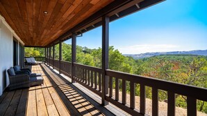A covered deck with a wooden ceiling and railing, overlooking a forested landscape.