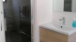 Une salle de bain avec un lavabo blanc, un miroir et un espace douche.