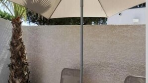 Deux fauteuils de jardin, un ventilateur de plafond et un parasol, le tout placé près d’un palmier et d’un mur blanc.