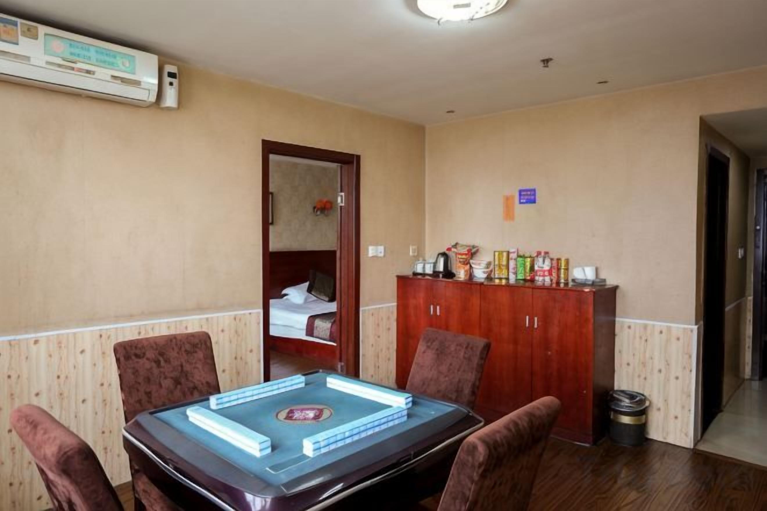 A hotel room with a dining table, chairs, a minibar, and a door leading to a bathroom.