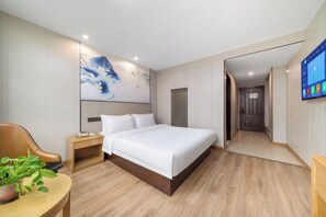 Quarto de hotel moderno com uma cama grande, uma mesa de cabeceira com abajur, televisão na parede e um quadro de grandes dimensões.