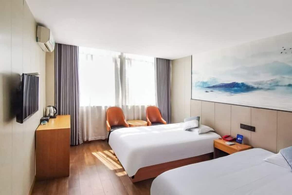 Quarto de hotel com duas camas, uma escrivaninha, uma cadeira, uma televisão e um quadro na parede.