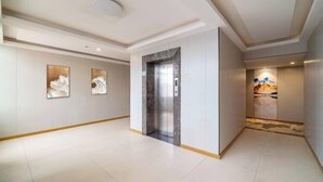 Een ruime hal met een moderne lift, witte muren en kunstwerken.